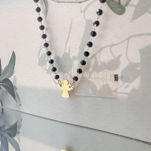 Close-up of black beaded necklace featuring a polished gold angel-shaped pendant