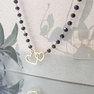 Detailed shot of a black beaded necklace featuring two interlocked golden heart pendants