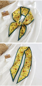 Détail d'un foulard en soie jaune à fleurs avec bordure verte porté sur une chemise blanche