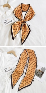 Macro detail of long orange silk scarf with black M-pattern and bow-knot styling