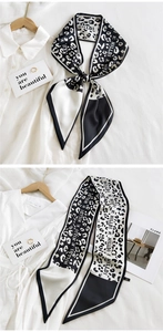 Detail of a leopard print silk scarf tied on a white shirt with brand logo and golden rings