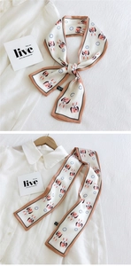 Détail d'un foulard twilly en soie imprimé avec motifs lapin et horloge sur satin crème