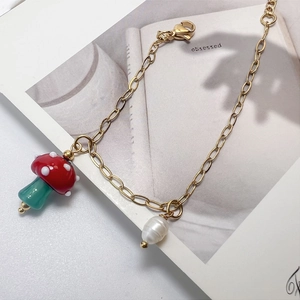 Detailed shot of a gold mushroom charm bracelet with a green stem and white pearl accent