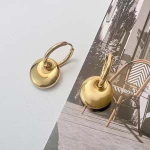 Close-up of golden hoop earrings with flat disc charms showing 18K gold-plated finish