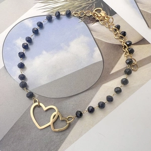 Close-up of bohemian black beaded bracelet with double hollow heart gold pendants