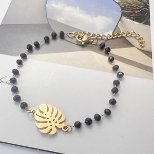 Macro detail of black beaded bracelet with gold monstera leaf charm and adjustable chain