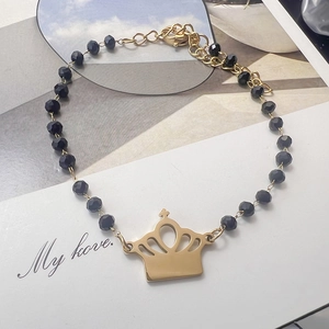 Detail view of black beaded bracelet featuring a golden crown pendant and lobster clasp