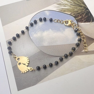 Detail of bohemian black bead bracelet featuring gold baby footprint charms and lobster clasp
