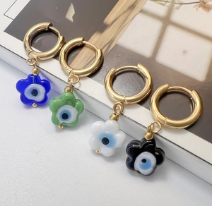 Close-up of gold hoop earrings with evil eye flower charms in blue, green, and white enamel