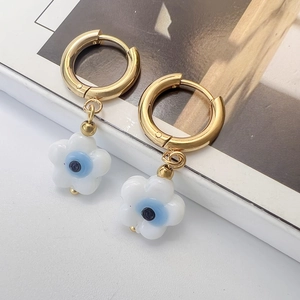 Detail of gold huggie earrings with white flower charms and blue evil eye accents