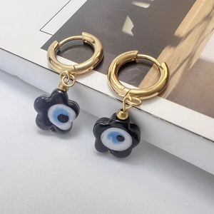 Detail view of golden hoop earrings featuring black flower charms and evil eye motifs