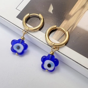 Detail shot of gold flower earrings with blue evil eye glass charms on white background
