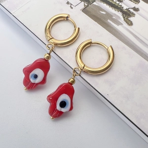 Détail de créoles dorées avec pendentifs main de Hamsa et breloques œil bleu en émail