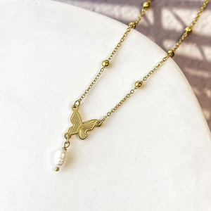 Dettaglio ravvicinato della collana a farfalla dorata con perla barocca su marmo