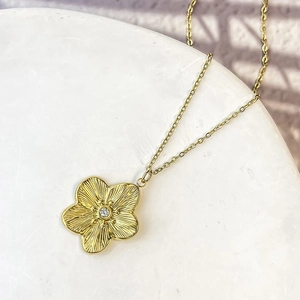 Vintage golden flower pendant necklace with central crystal on white marble surface