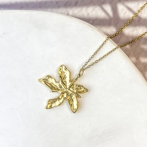 Détail du pendentif feuille dorée avec texture martelée sur une chaîne délicate