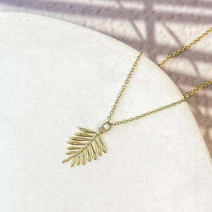 Vue détaillée du pendentif feuille de palmier dorée avec texture métallique et chaîne fine