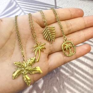 Détail de pendentifs tropicaux dorés incluant palmier et hibiscus sur des chaînes fines