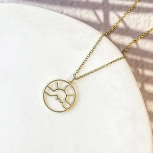 Détail macro du collier doré en acier inoxydable avec pendentif découpé montagne soleil