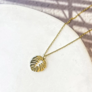 Gros plan du collier avec pendentif feuille de monstera doré sur marbre blanc