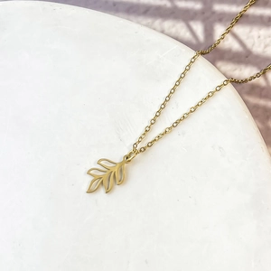 Gros plan détaillé d'un collier pendentif feuille d'or sur un présentoir en pierre