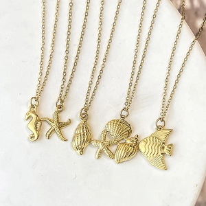 Gold stainless steel ocean necklaces featuring sea star and shell pendants on stone tray