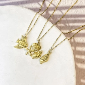 Gold stainless steel starfish and seashell pendant necklaces on white marble base