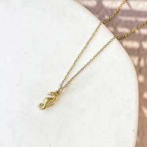 Close-up of gold seahorse pendant necklace on white podium with soft shadows