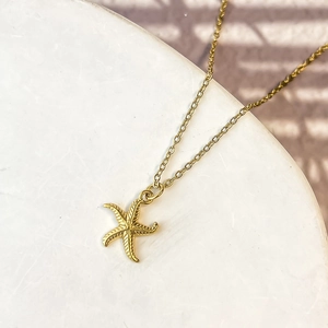 Close-up of golden starfish pendant necklace with detailed woven texture on white marble