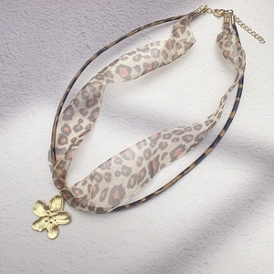 Detail of leopard print chiffon ribbon and gold flower pendant on a layered necklace