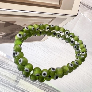 Dettaglio macro di perline evil eye verdi da 6 mm su un braccialetto elastico con riflessi
