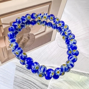 Detailed view of handmade blue glass bead bracelet with white daisy flower patterns