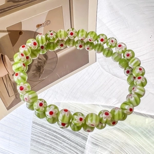 Detailed view of green glass beads with white daisy patterns and red centers on a bracelet