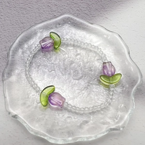 Minimalist tulip beaded stretch bracelet with purple glass flower charms on a tray