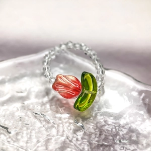 Detail of beaded ring with red tulip flower and clear glass beads on a wave glass surface