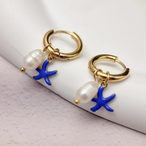Detail of gold starfish and baroque pearl dangle earrings on a white minimalist display stand