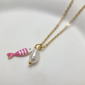 Macro detail of gold necklace with a pink fish charm and a white baroque pearl pendant