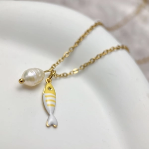 Macro shot of gold stainless steel necklace with freshwater pearl and fish charms