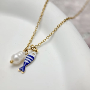 Detail of gold necklace featuring baroque pearl and blue striped fish enamel pendant