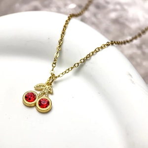 Collier minimaliste avec pendentif cerise rouge et chaîne dorée sur plateau en céramique
