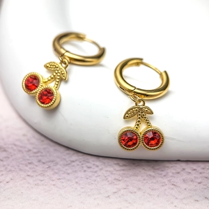 Boucles d'oreilles cerises dorées avec cristaux rouges sur un présentoir à bijoux