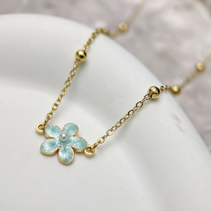 Macro detail of gold necklace featuring light blue enamel flower pendant and small white pearl