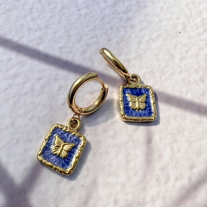 Macro detail of 18K gold butterfly earrings with blue enamel in a square drop design