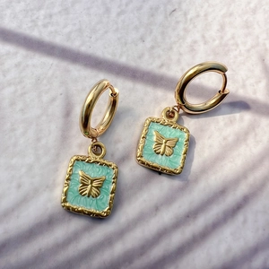 Close-up of 18K gold earrings with green enamel and butterfly pendants on stone texture