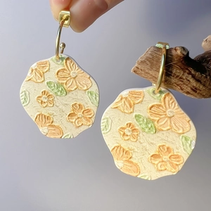 Detail handgefertigter cremefarbener Blumenohrringe mit orangefarbenen Blütenblättern