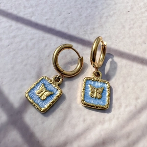 Detail of 18K gold hoop earring featuring a light blue enamel square butterfly pendant