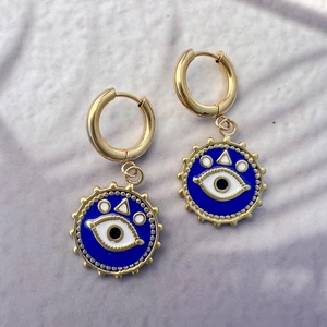 Détail des boucles d'oreilles en acier doré avec pendentifs œil bleu émaillé