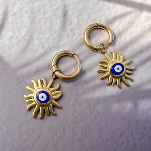 Détail de boucles d'oreilles soleil avec œil bleu doré sur une surface en pierre texturée