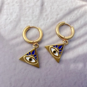 Détail de boucles d'oreilles œil maléfique dorées sur fond de tissu lilas