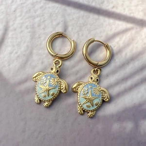 Detailed view of 18K gold-plated turtle earrings with blue enamel and sea shell charms